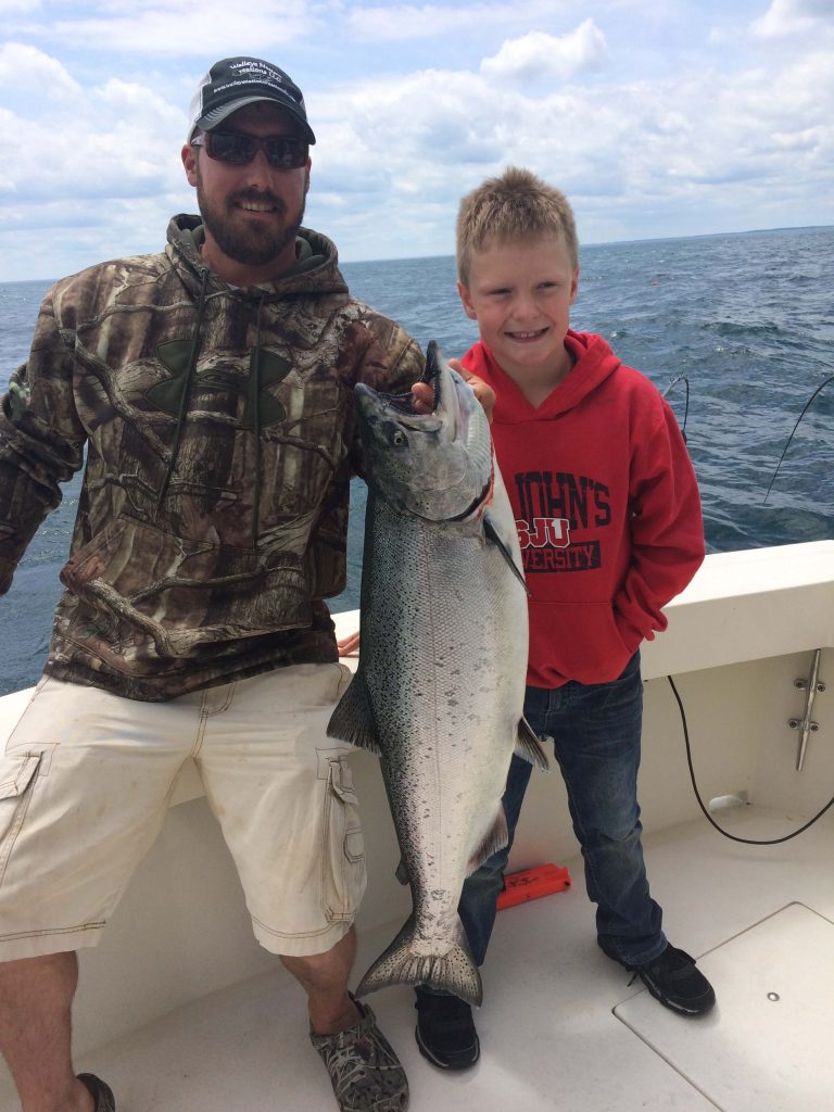 Man holding up Steelhead next to little boy in red sweatshirt, charter fishing on Lake Michigan