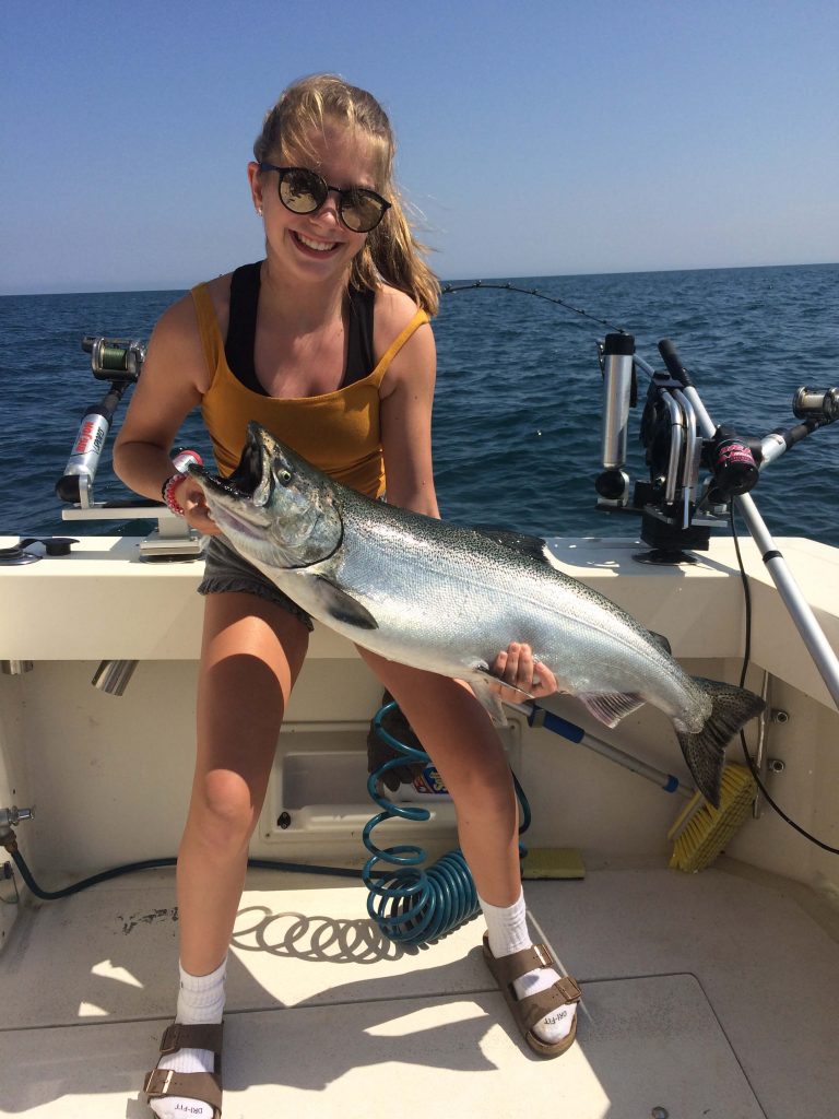 teen girl holding up sturgeon bay king salmon on charter fishing boat